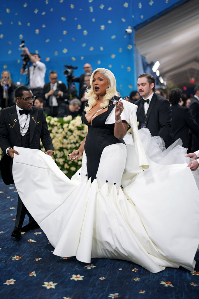 Lizzo is wearing a black and white dress and holding a cigarette extender.
