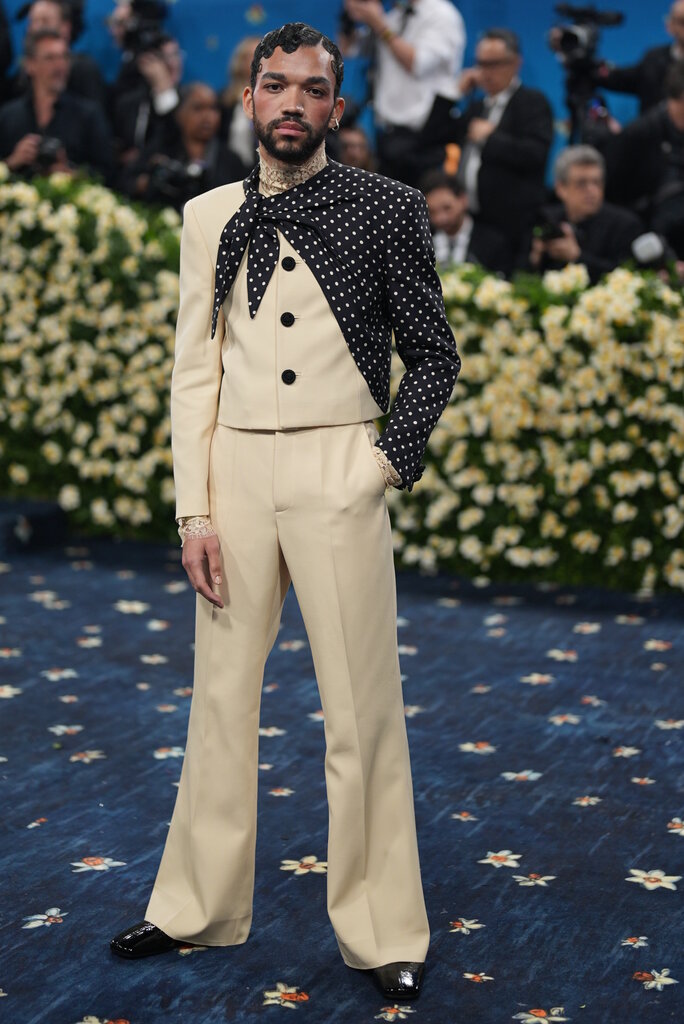 Justice Smith is wearing a tan suit with black and white polka dot details on one sleeve.