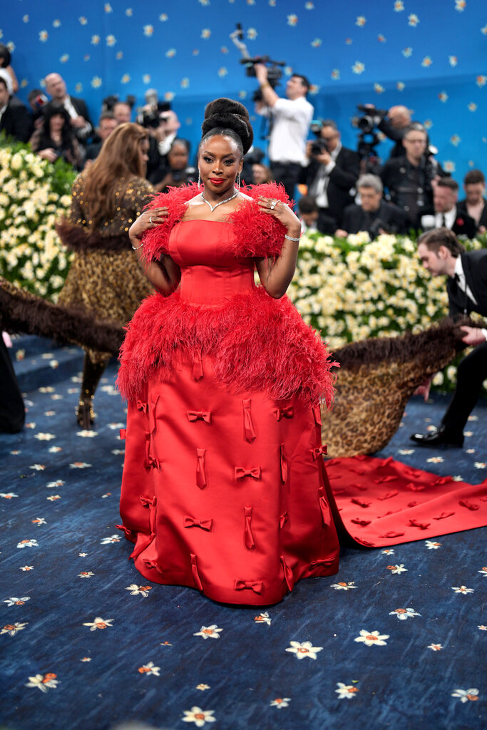Chimamanda Ngozi Adichie wearing a red floor-length gown with bow embellishments and feather detailing.