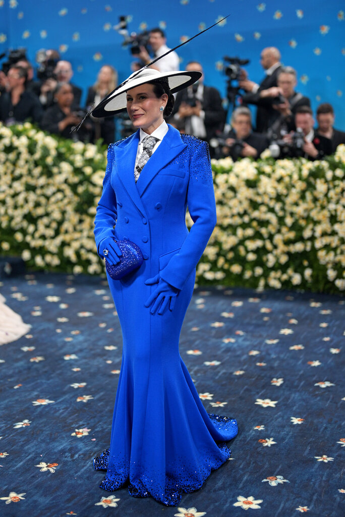 Jamie Singer Soros wearing a blue floor-length blazer gown, with a wide-brim black and white hat.
