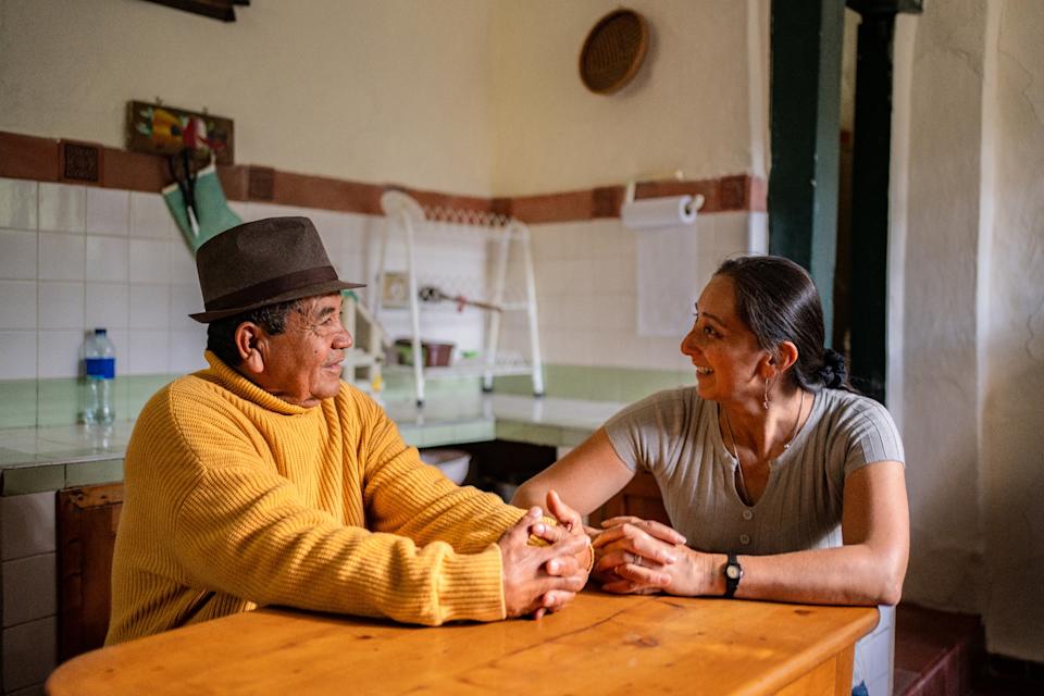 Two people sit at a kitchen table, smiling and engaging in a friendly conversation
