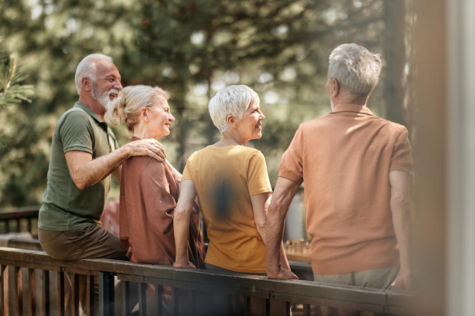 Four older adults enjoying nature on a wooden deck, engaged in conversation and laughter