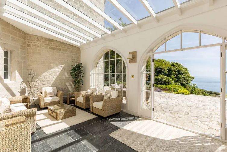 Sunlit conservatory with wicker furniture and ocean view.