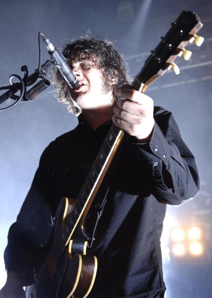 A musician singing into a microphone while playing an electric guitar.