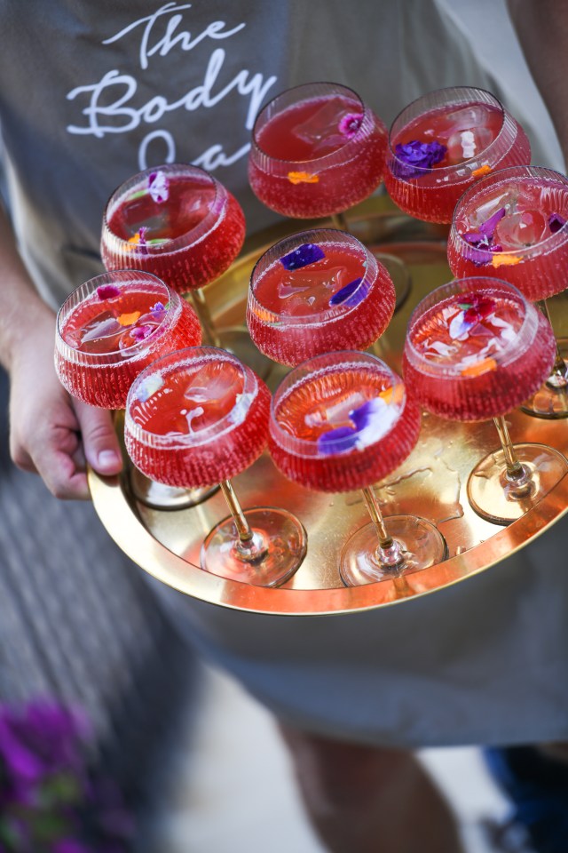 Person holding a tray of red cocktails garnished with flowers.