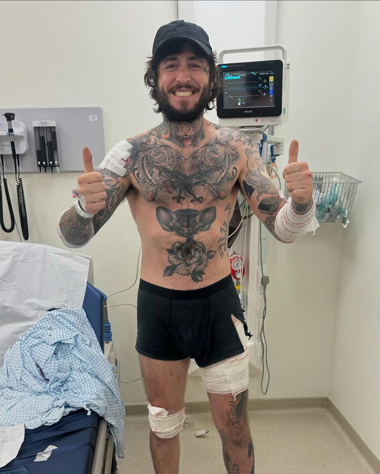 A tattooed man in a hospital room gives a thumbs-up.