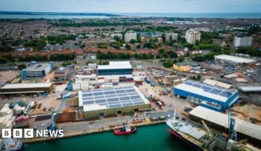 An aerial shot of Portsmouth International Port an area with boats, cranes and warehouse facilities and the city in the background