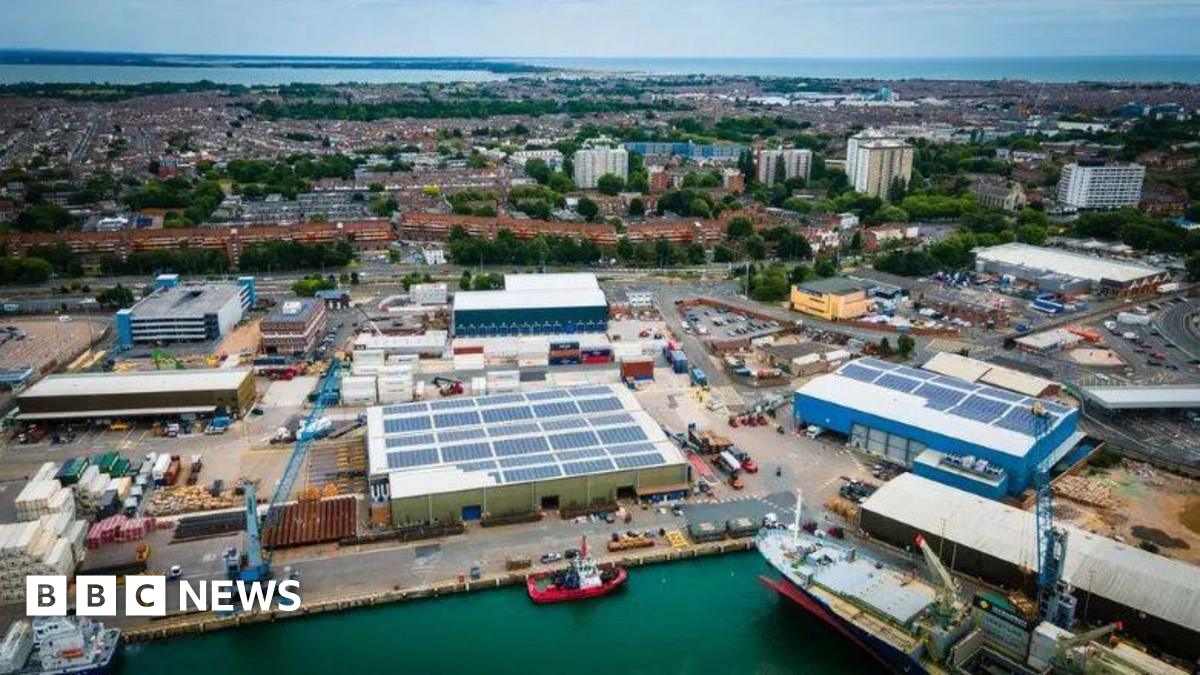 An aerial shot of Portsmouth International Port an area with boats, cranes and warehouse facilities and the city in the background