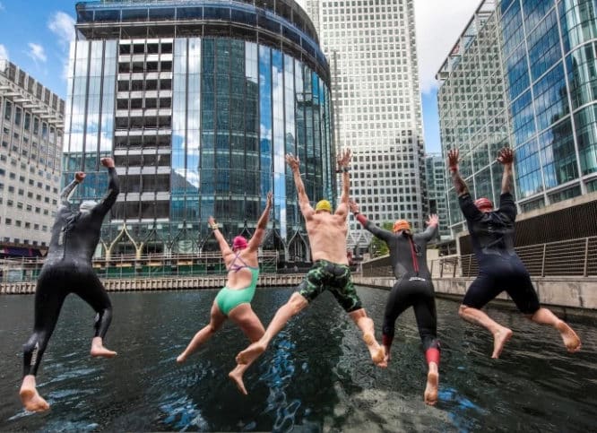 a group of swimmer jumping into the water at canary wharf, arms and legs stretched out