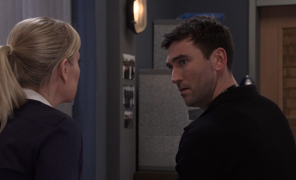 coronation street, kit green looking worried, in the police station in a black top