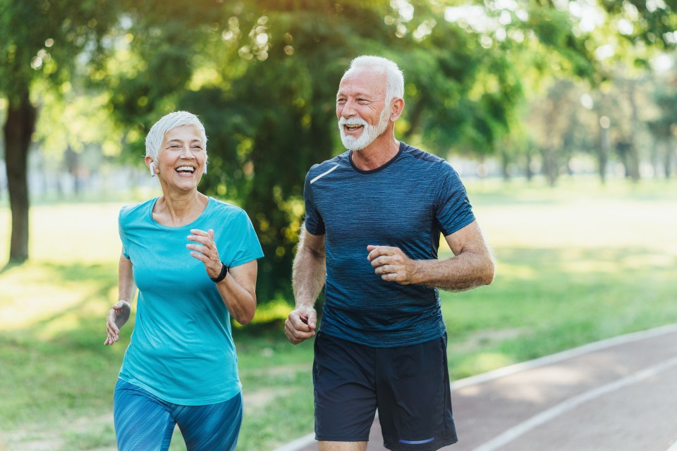 Smiling senior couple jogging together in a park.