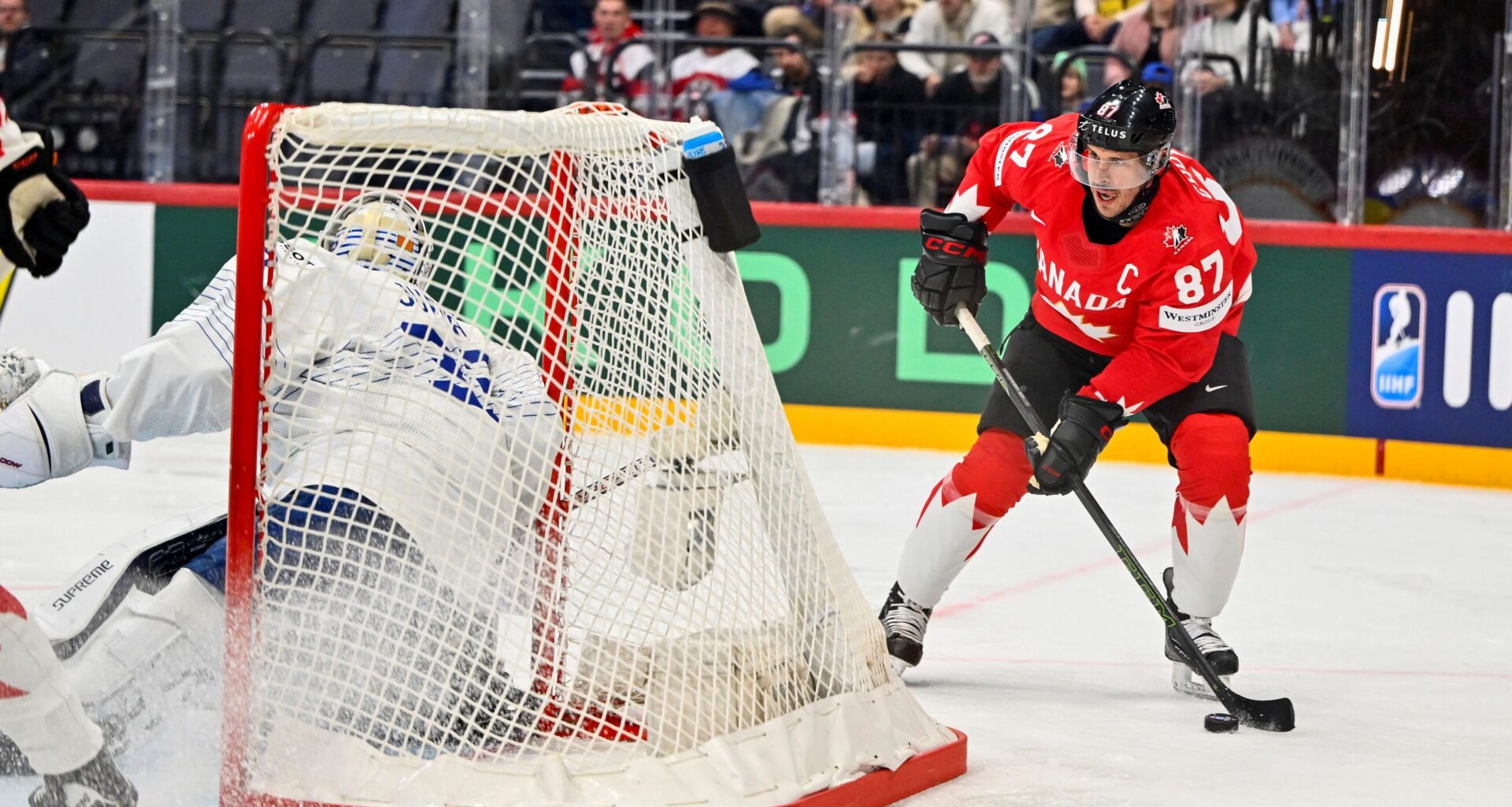 Sidney Crosby plays the puck behind the next while wearing a red Team Canada jersey