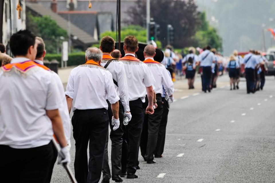 Men in white shirts and orange sashes walk down a road.
