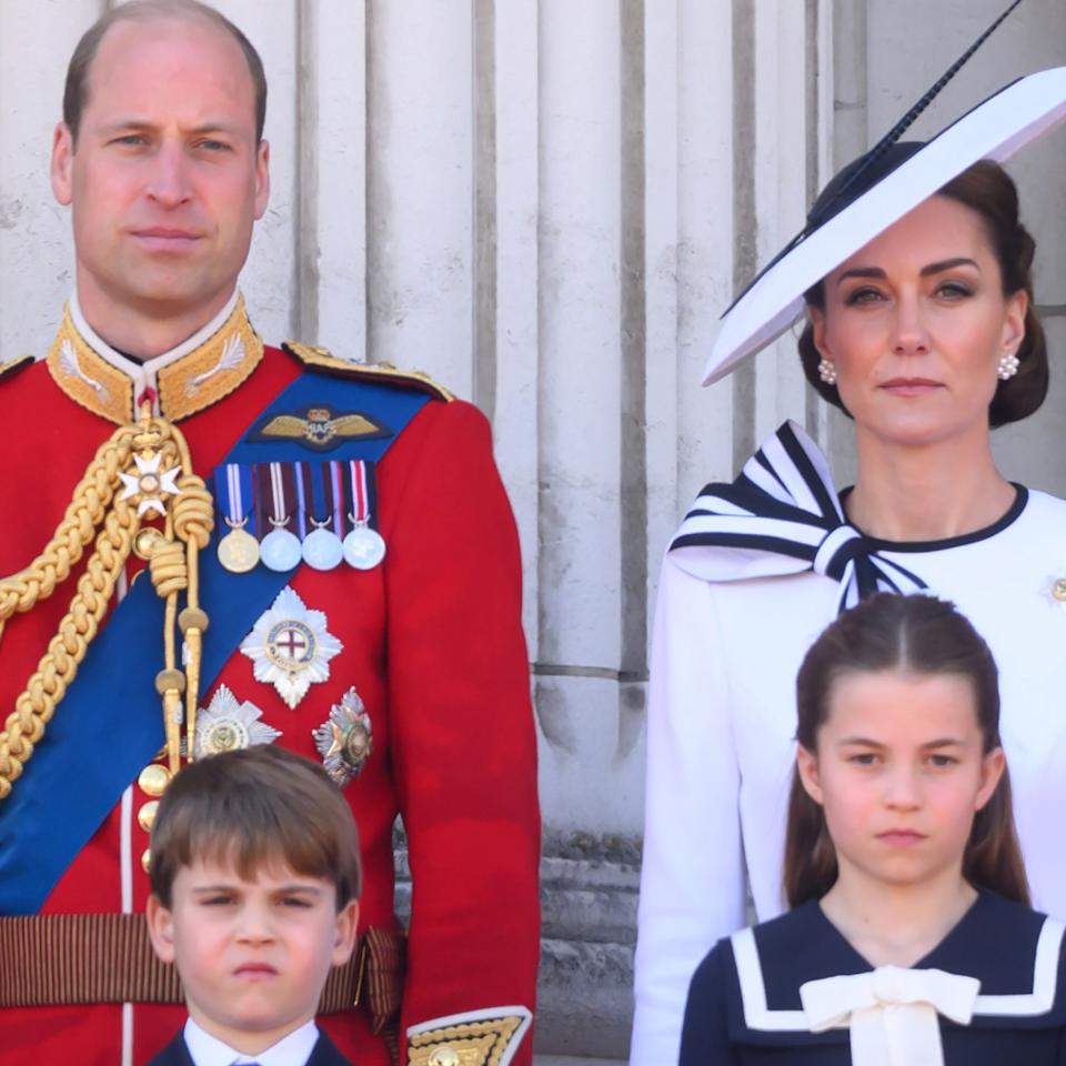  Prince William wears red military uniform and Kate Middleton wears a white dress with navy detailing, as they stand on the Buckingham Palace with their three kids, Prince George, Prince Louis, and Princess Charlotte. 