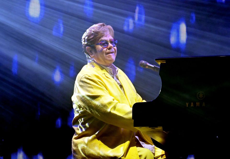 Elton John performing onstage at a piano.