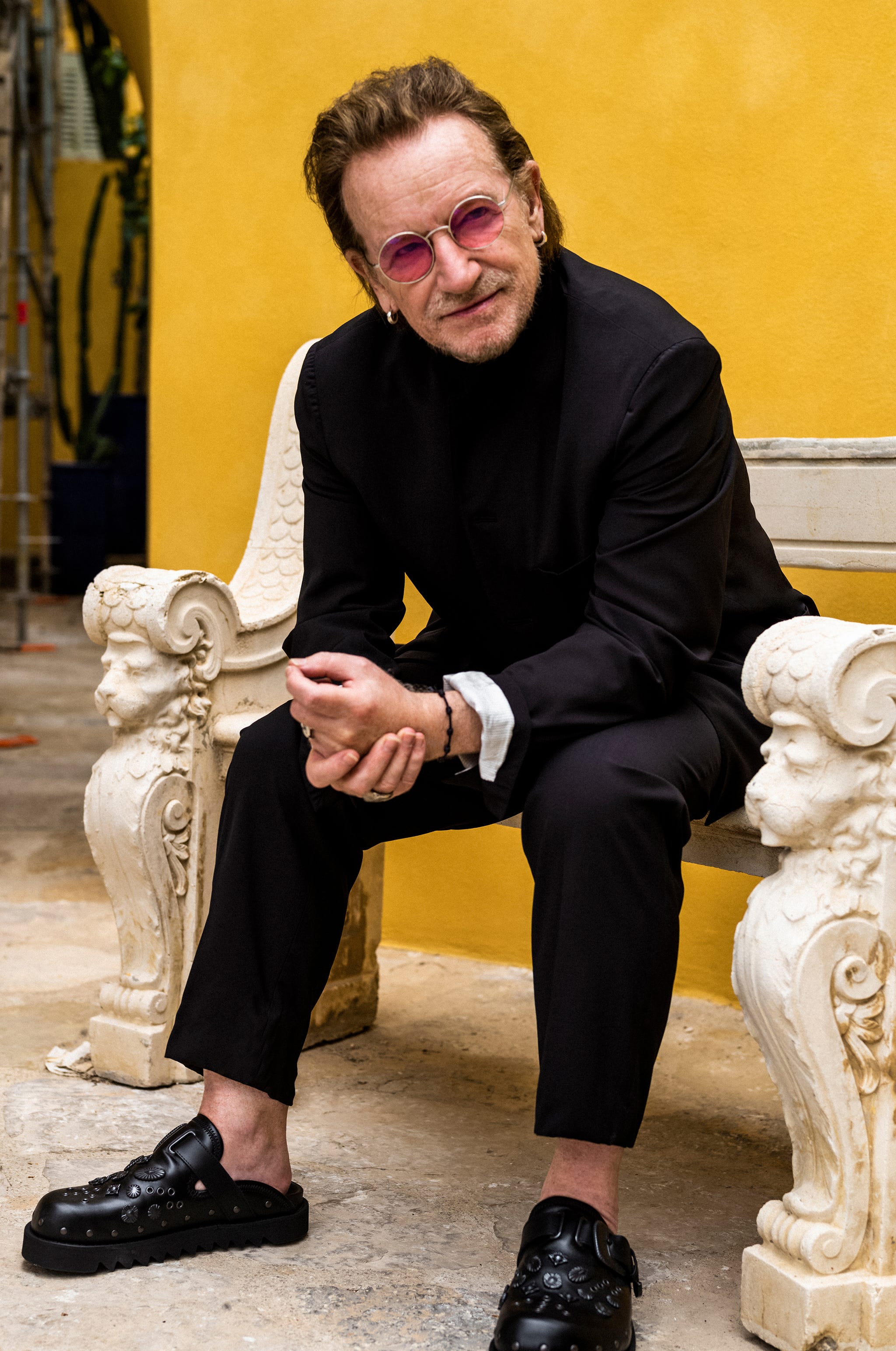 a person seated on a decorative stone bench in a vibrant yellow setting wearing stylish casual clothing