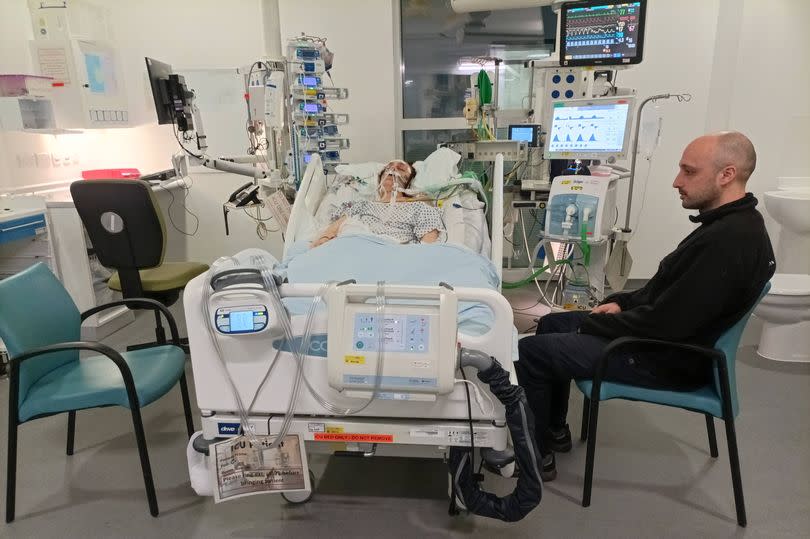 Anna lying in a hospital bed in the ICU while her brother sits beside in a chair