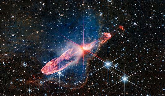 A small bright red star in the centre in the process of forming as it illuminates a thick swirling  ring of gas around it a deep red. In the background are a fiel dof stars