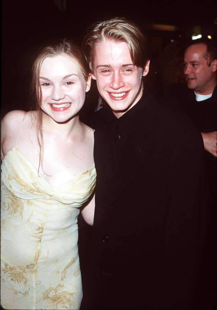 Two celebrities smiling at an event; one wearing a floral-patterned dress, the other in a dark suit