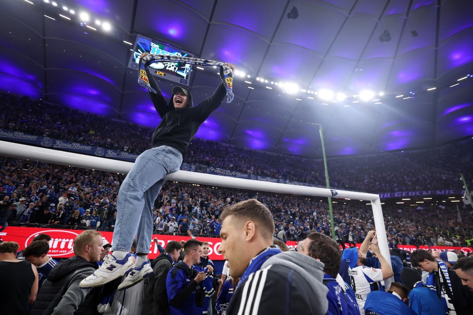 A fan celebrates on the goalpost after a soccer match.