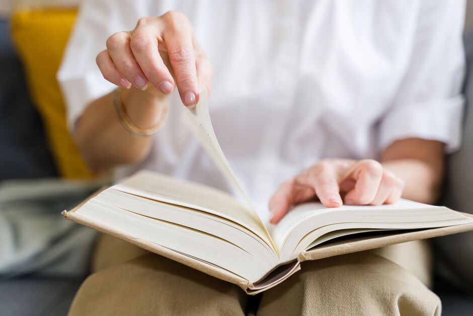 Senior woman turning page of a book while reading on the sofa