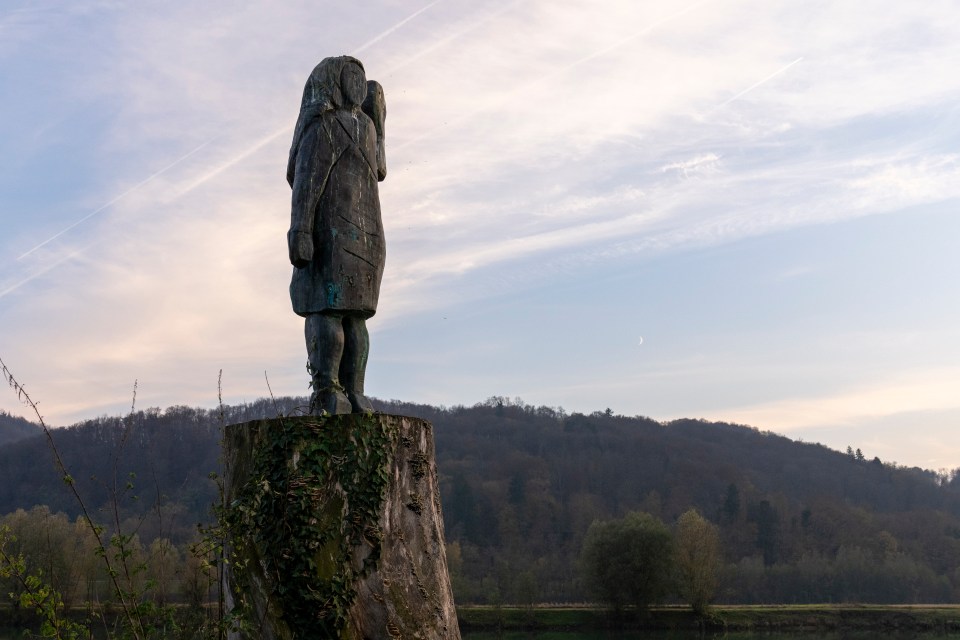 Bronze sculpture of a woman on a tree stump overlooking a river and hills.