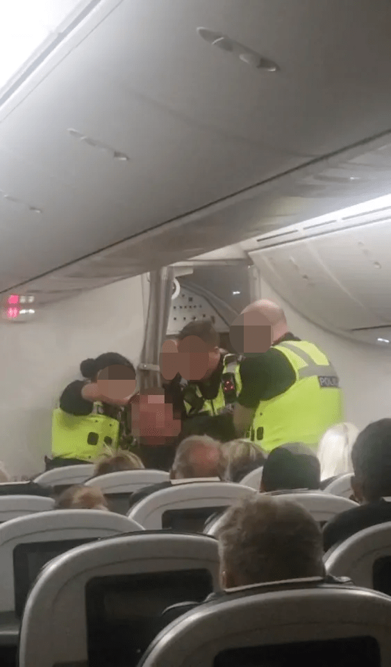 Police officers arresting a disruptive passenger on an airplane.