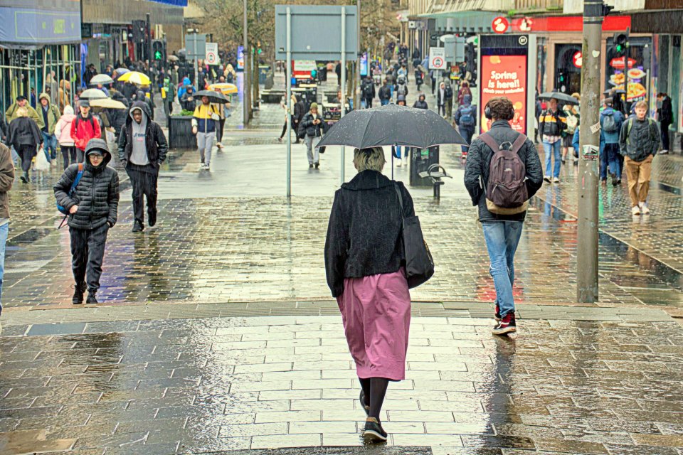 People sheltering under umbrellas in heavy rain on a city street.