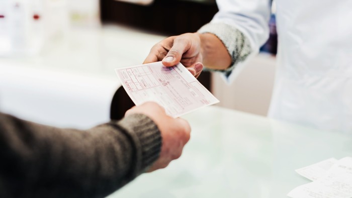 A person hands a paper prescription to another person across a counter