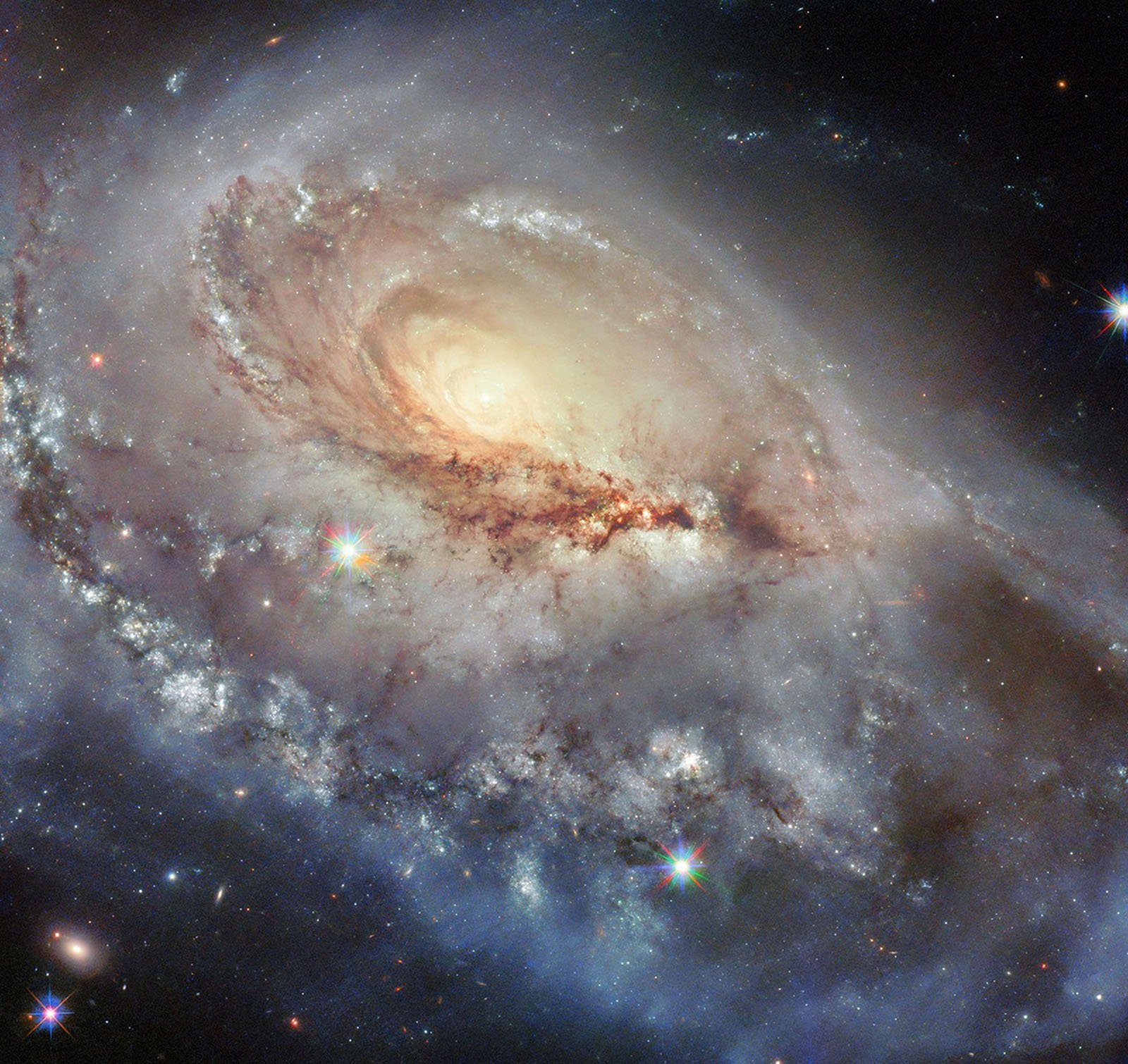 A bright spiral galaxy with a glowing yellow center, swirling arms of stars and dust, and several colorful starbursts scattered throughout, set against a dark background speckled with distant stars.