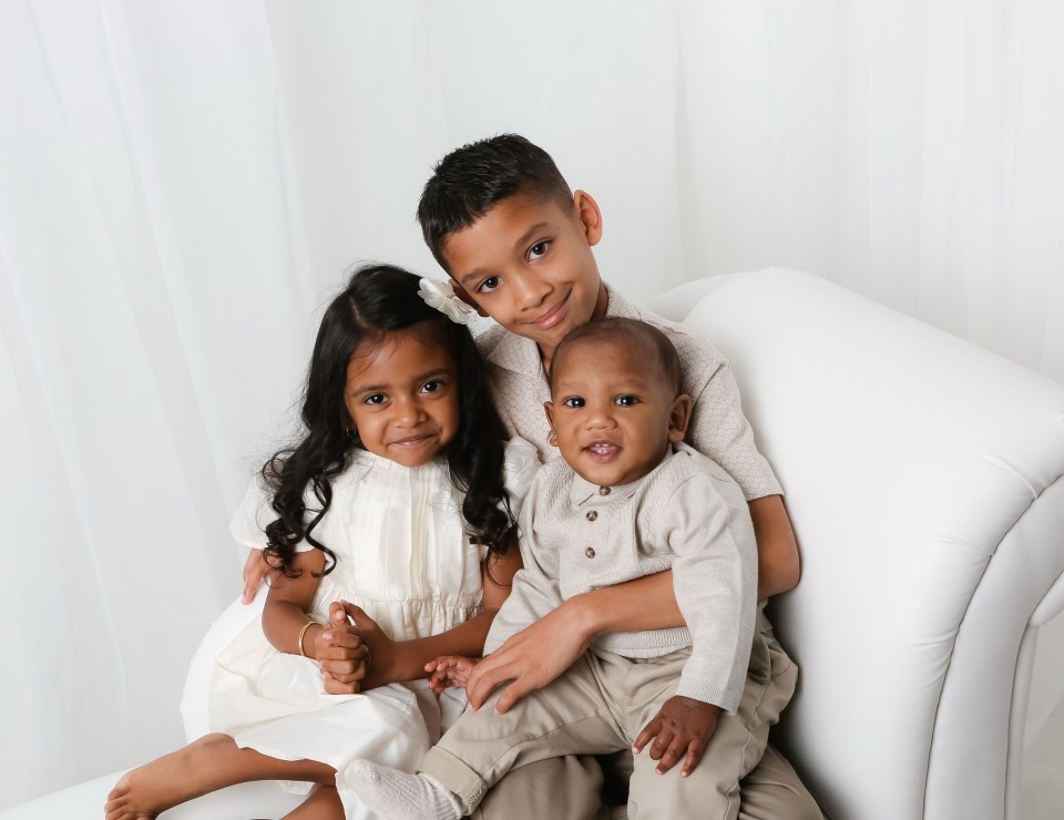Three young siblings sitting together on a white couch.