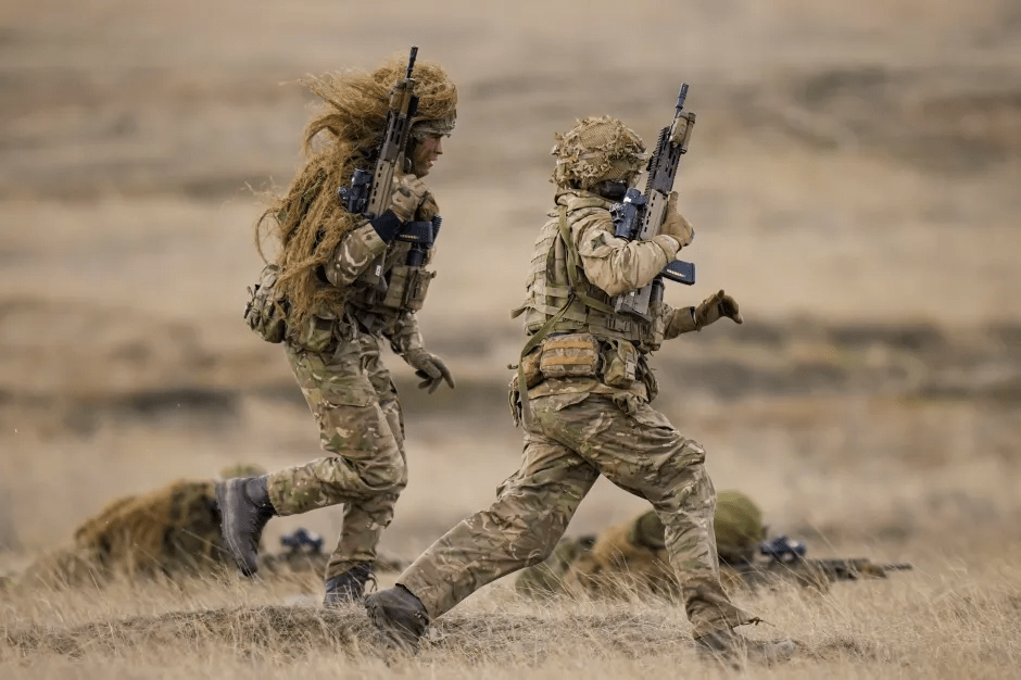 Two soldiers running through a field, carrying rifles.