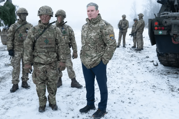 A man in civilian clothes stands with soldiers in camouflage uniforms in a snowy field.