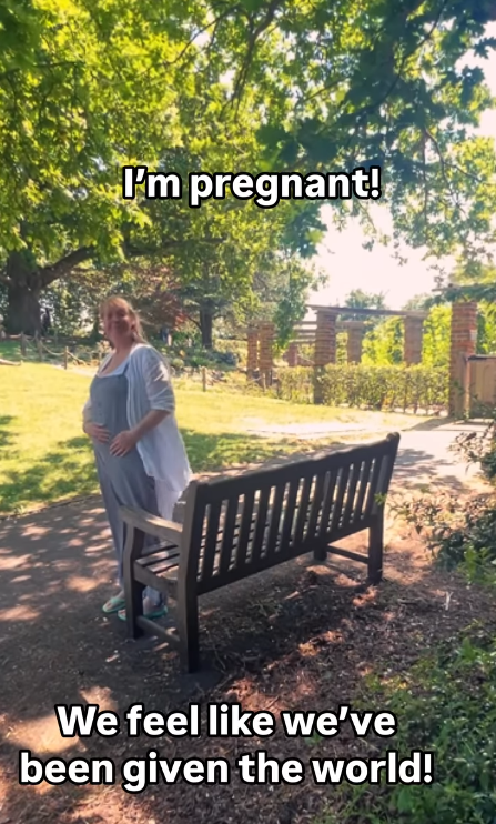 Pregnant woman standing by a park bench, announcing her pregnancy.