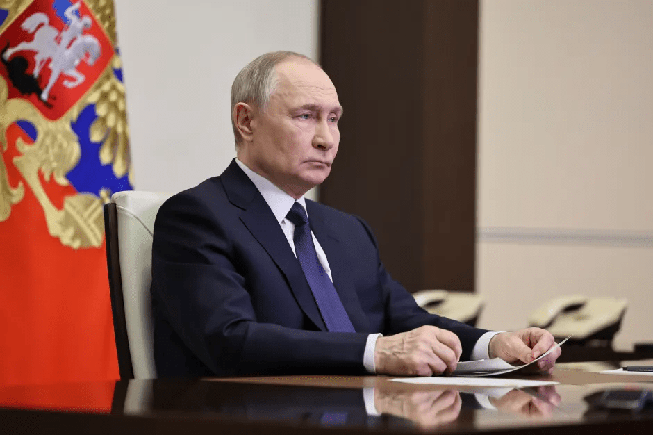 Vladimir Putin sitting at a table reviewing documents.