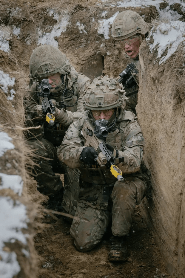 Three soldiers in camouflage uniforms crouched in a trench, aiming their rifles.