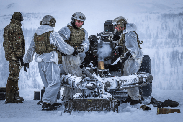 Soldiers in white camouflage operating a howitzer in snowy conditions.