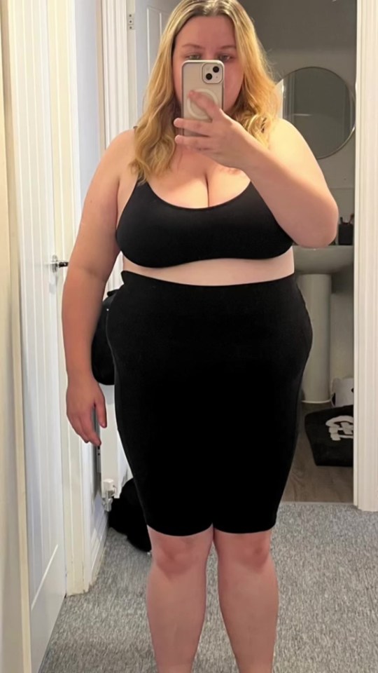 Woman in black top and shorts taking a selfie.