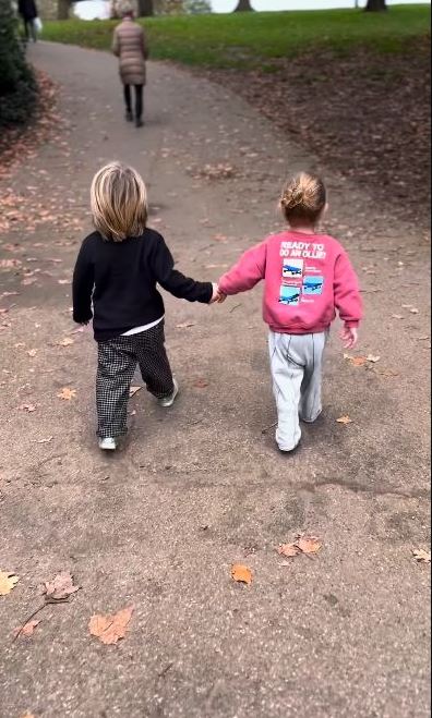 Two young children holding hands and walking down a path.