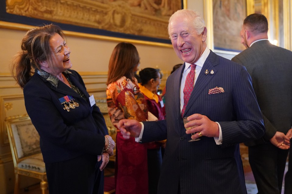 King Charles III laughing and talking to a woman at a reception.