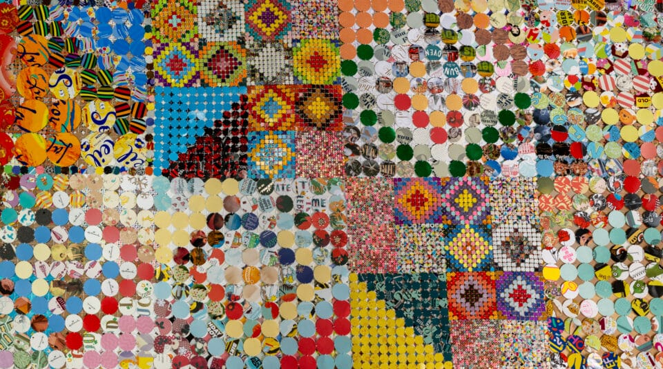 a detail of an artwork comprising cloth made from woven and connected pieces of plastic and paper, creating colorful patterns