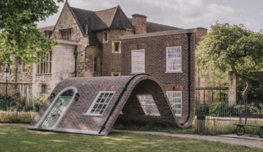 alex chinneck’s brick facade sculpture sits down in london