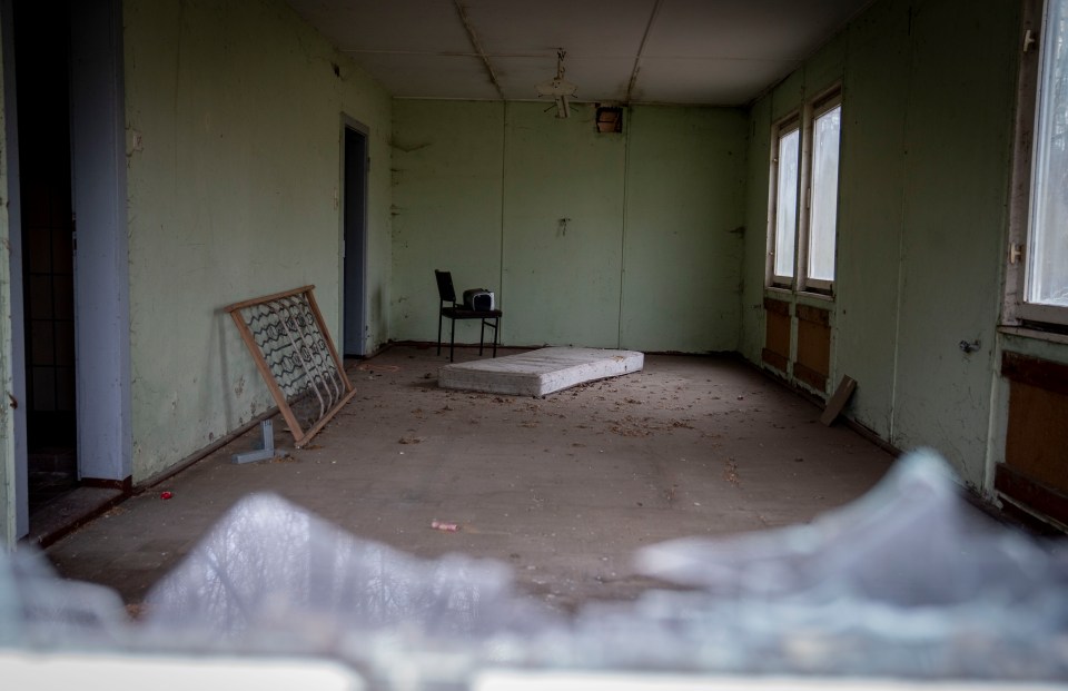 Interior of dilapidated room with mattress, chair, and bed frame.