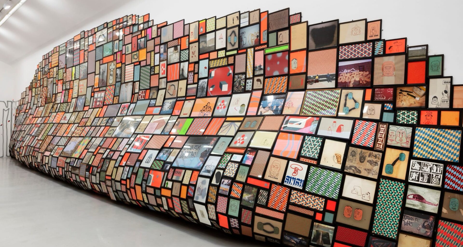 a large-scale installation along a white gallery wall, which looks like a giant slumped surface that is completely covered in a grid of tiny images