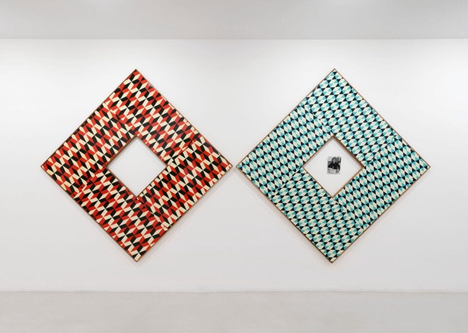 two square geometric paintings, one green and one orange, situated next to each other in a white-walled gallery space