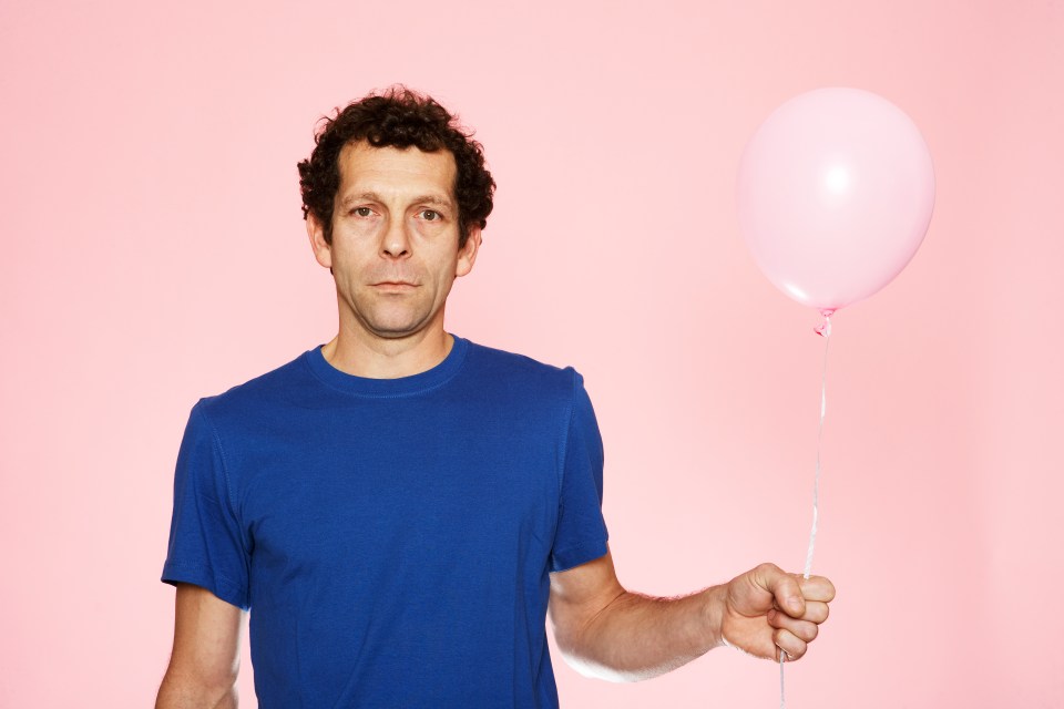 A middle-aged man in a blue shirt holds a pink balloon.