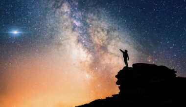 Astronomers respond: lone person standing on top of rock, pointing with hand towards the Milky Way and the vast expanse of universe.