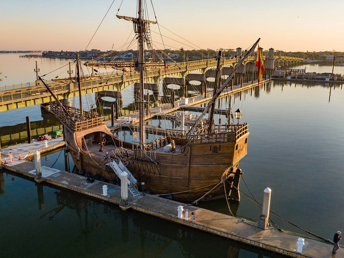 a historic ship replica docked at a port, with its sails tied up