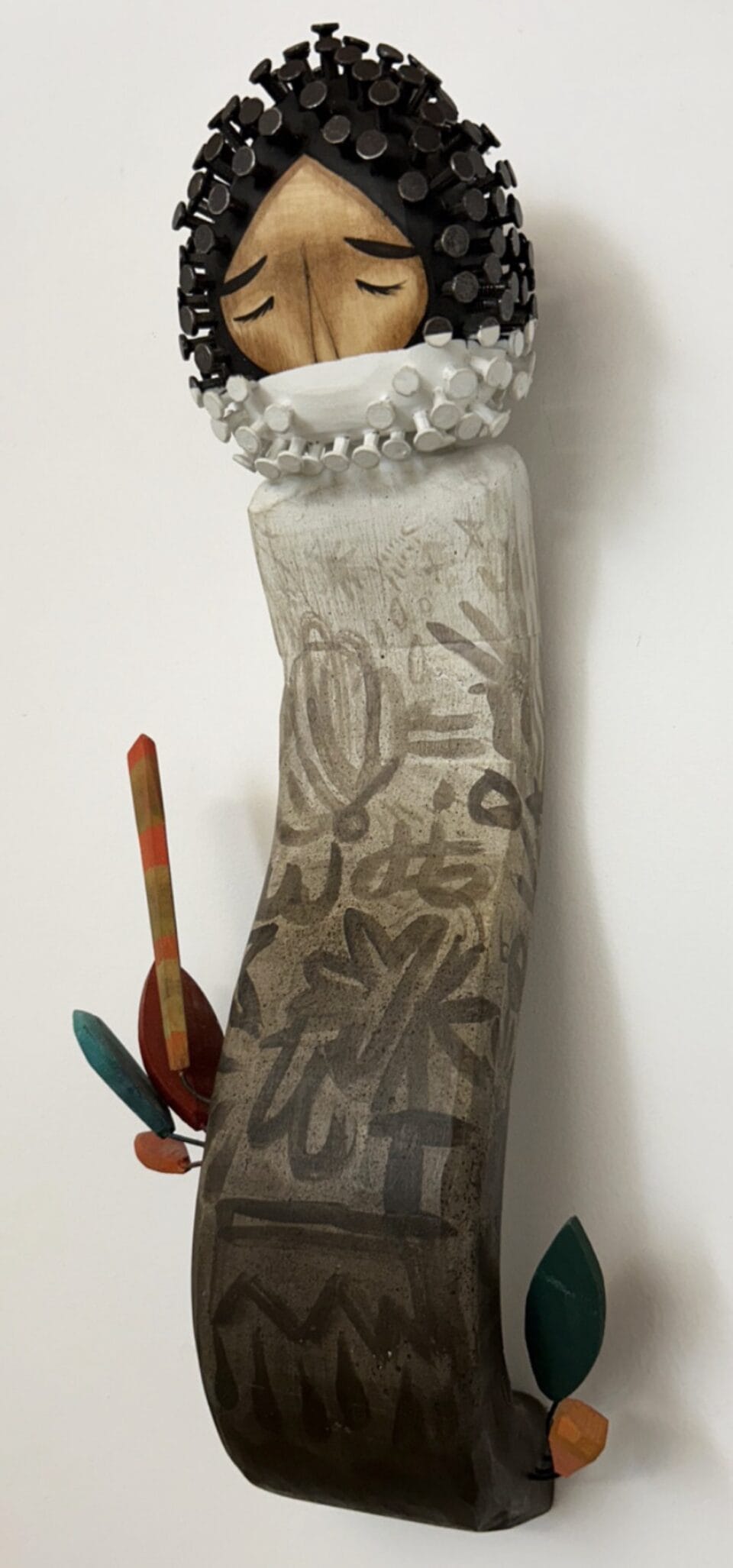 a wall sculpture made of carved wood of an abstract figure, with a head that has nails for hair