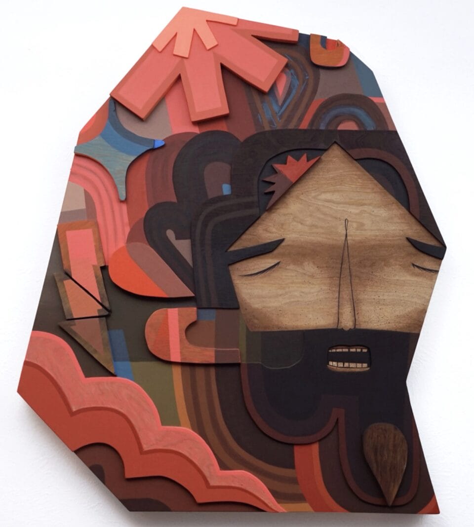 a wooden artwork featuring a man with a beard, with his eyes closed, with a red, pink, and brown geometric pattern on his hair or hood